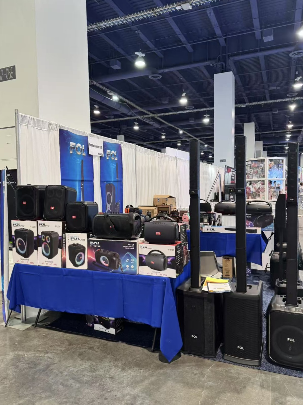 Espacio de exhibición de FOL Audio en ASD 2025, mostrando diversos modelos de altavoces: unidades Bluetooth compactas, sistemas PA de gran formato y accesorios de audio, dentro de un stand de feria comercial.